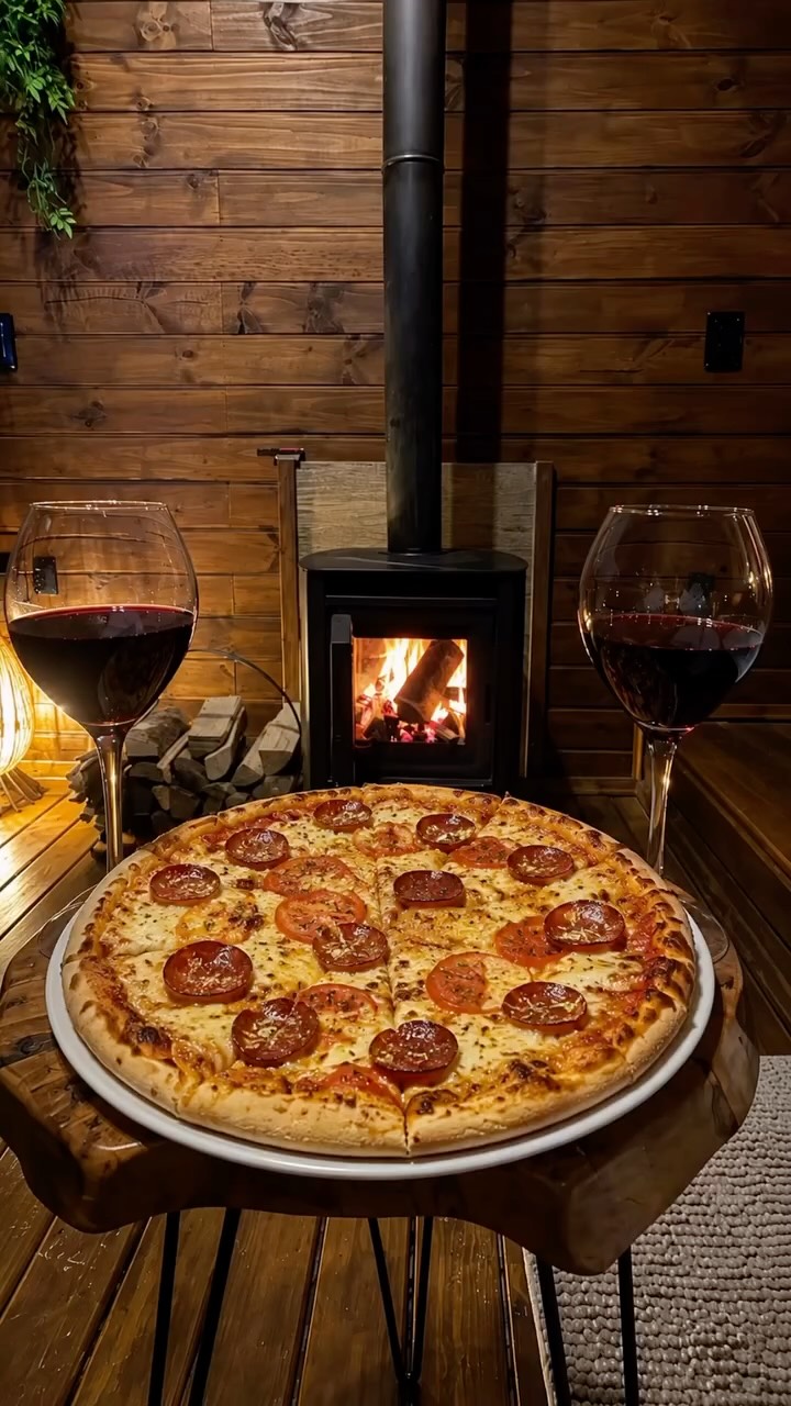 Pizza e taças de vinho diante da lareira acesa