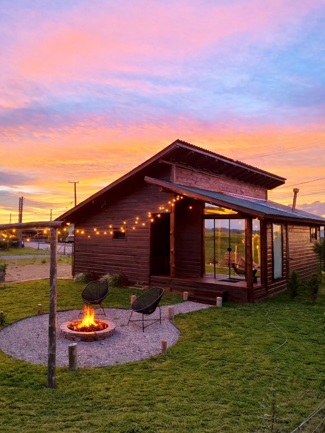 Cabana de madeira com varal de luzes e fogueira ao entardecer